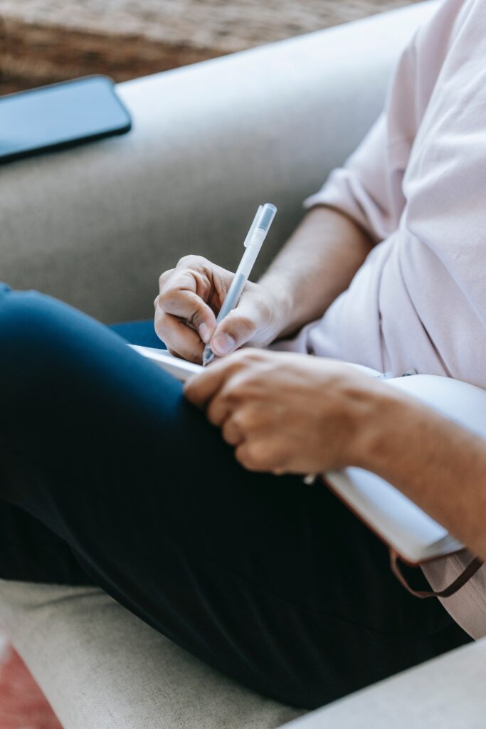 White, masculine figure leaning back on couch writing notes on paper.